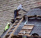 Man installing roofing slate on a round turret on a church.